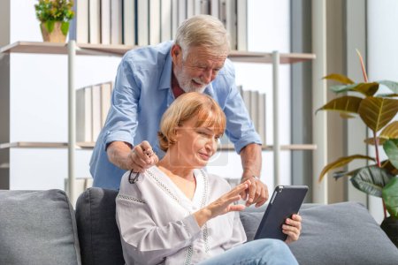 Téléchargez les photos : Couple plus âgé dans le salon, Femme et un homme utilisant smartphone parler sur appel vidéo, concept de famille heureux - en image libre de droit