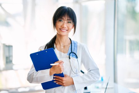 Photo for Smiling confident female doctor holding clipboard posing in hospital. Medicine, profession and healthcare concept - Royalty Free Image