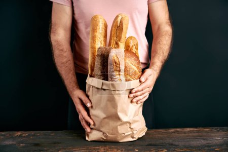 Man holds fresh loaves of bread baguettes in paper bag over light background. Bakery, food concept