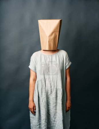 Foto de Mujer en vestido largo con una bolsa de papel en la cabeza de pie sobre fondo oscuro - Imagen libre de derechos