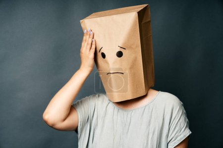 Woman with hand on head and upset smile on the paper bag on head. Bad memory, emotions concept.
