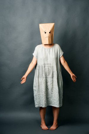 Verwirrte Frau mit Papiertüte über dem Kopf auf dunklem Hintergrund. Emotionales Konzept