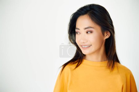 Photo for Young smiling asian woman with braces looking aside to copy space on white studio background - Royalty Free Image