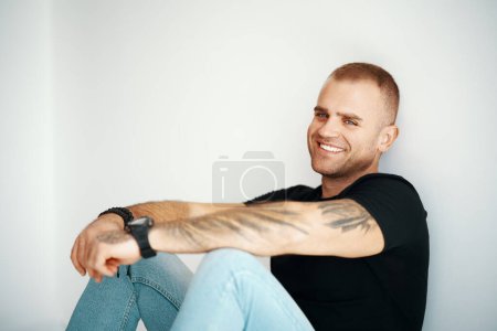 Smiling handsome man sitting on floor looking to camera with copy space. Male beauty concept