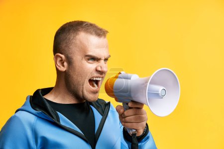 Junger wütender Mann schreit laut und hält Megafon über gelbem Hintergrund