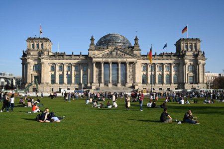 Foto de Berlín, Alemania - 31 de octubre de 2022: La gente se relaja en el gras cerca del Bundestag alemán (edificio del Reichstag) es el parlamento nacional de la República Federal de Alemania. - Imagen libre de derechos