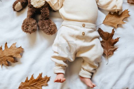 Photo for Baby feet in beige pants among autumn yellow leaves on a white background. Autumn background. - Royalty Free Image