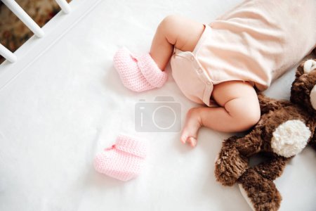 Neugeborenes Mädchen in Strickschuhen mit Schleife auf einer weißen Decke. Baby verlor Schuhe. Kindheitskonzept.