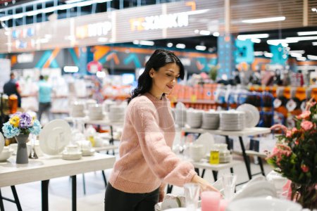 Téléchargez les photos : Une jeune femme brune en pull rose achète de la vaisselle dans un magasin. - en image libre de droit