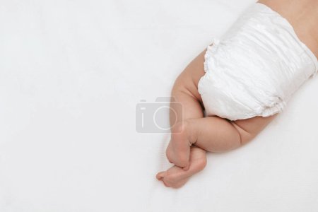 Photo for Newborn baby legs in a white nappy on the bed. Top view. Baby skin care and diaper change. - Royalty Free Image