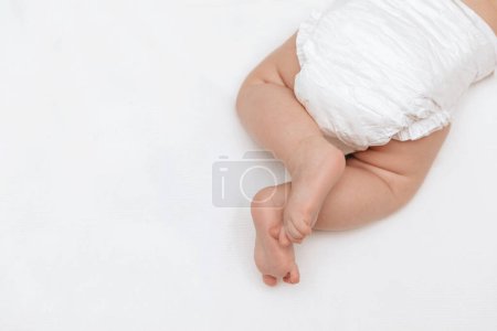 Foto de Patas de bebé recién nacidas en pañales blancos en la cama. Vista superior. Cuidado de la piel del bebé y cambio de pañal. - Imagen libre de derechos