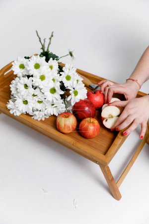 Photo for Red apples in the hands of a woman, on a wooden tray with white flowers on a white background. - Royalty Free Image