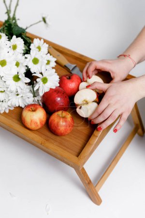 Téléchargez les photos : Pommes rouges dans les mains d'une femme, sur un plateau en bois avec des fleurs blanches sur un fond blanc. - en image libre de droit