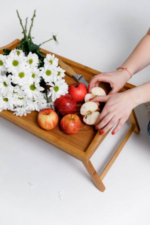 Foto de Manzanas rojas en las manos de una mujer, sobre una bandeja de madera con flores blancas sobre un fondo blanco. - Imagen libre de derechos