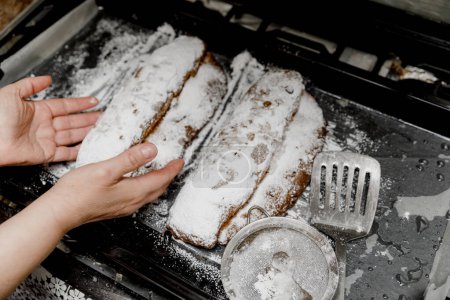 Foto de Panes Stollen tradicionales alemanes espolvoreados con azúcar en polvo en una bandeja para hornear en manos femeninas. - Imagen libre de derechos