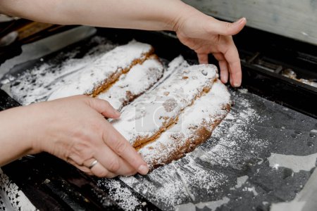 Photo for German traditional Stollen breads sprinkled with powdered sugar on a baking sheet in female hands. - Royalty Free Image