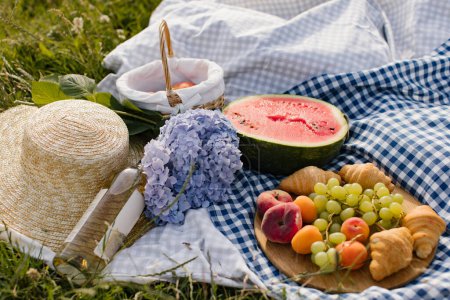 Foto de Desayuno picnic con croissants, frutas y flores en una manta en un día soleado. Picnic, comida, brunch, humor de verano. - Imagen libre de derechos