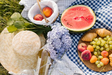 Foto de Desayuno picnic con croissants, frutas y flores en una manta en un día soleado. Picnic, comida, brunch, humor de verano. - Imagen libre de derechos