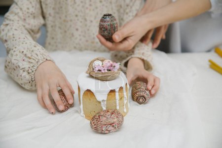 Téléchargez les photos : Gâteau de Pâques à glaçure blanche avec un nid d'oiseau décoratif avec des œufs et des fleurs. Œufs de Pâques en bois peint à la main dans les mains. - en image libre de droit