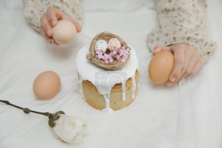 Foto de Pastel de Pascua con glaseado blanco con un nido de aves decorativo con huevos y flores en las manos de los niños. Niño está sosteniendo pastel de Pascua. - Imagen libre de derechos