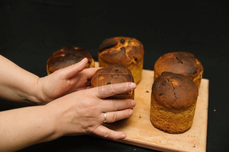 Freshly baked Easter cake in female hands on a black background. Easter cakes without decorations on a wooden board on a black background. Easter cakes cools down.