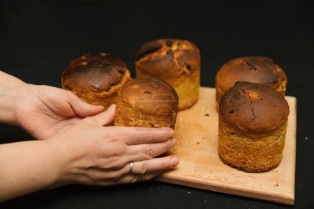 Frisch gebackener Osterkuchen in Frauenhand auf schwarzem Hintergrund. Osterkuchen ohne Dekoration auf einem Holzbrett auf schwarzem Hintergrund. Osterkuchen kühlt ab.