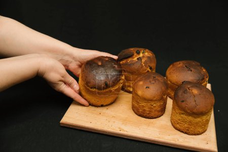 Frisch gebackener Osterkuchen in Frauenhand auf schwarzem Hintergrund. Osterkuchen ohne Dekoration auf einem Holzbrett auf schwarzem Hintergrund. Osterkuchen kühlt ab.