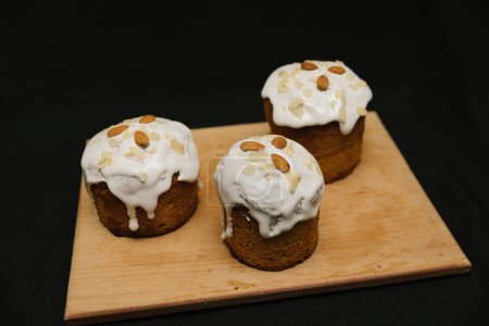 Téléchargez les photos : Gâteaux de Pâques avec glaçage blanc et noix d'amande sur une planche en bois sur fond noir. - en image libre de droit