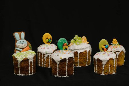 Téléchargez les photos : Gâteaux de Pâques avec glaçage blanc et décorations colorées pour enfants sur fond noir. - en image libre de droit