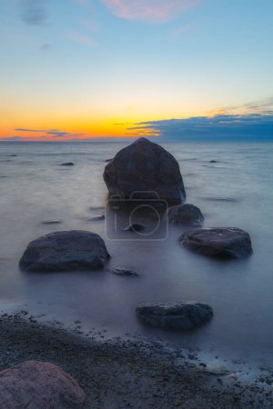 Heure bleue après le coucher du soleil sur la mer Baltique rocheuse coût. Petites pierres et gros rochers dans la mer. Photo longue exposition.