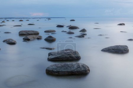 Blue hour after sunset. Smooth water and erratic boulders. Calm sea water. Long exposure