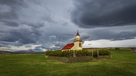 Kleine elegante historische Kirche in Island unter stürmischem Himmel.