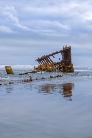 Wreck of the Peter Iredale along pacific coast in Oregon on a cloudy day with reflection.