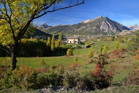 Photo for The chapel of Villard Saint Pancrace, located on a hill near Briancon, Hautes Alpes (French Southern Alps), France, surrounded by Autumn colors and with the town of Briancon in the background - Royalty Free Image