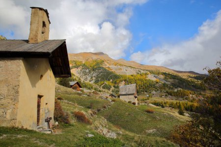 Photo for The hamlet Le Villard located along the Cristillan valley above Ceillac village, Queyras Regional Natural Park, Southern Alps, France, with Sainte Barbe chapel, a traditional wooden chalet and Autumn colors - Royalty Free Image