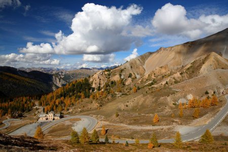 Foto de Colorido paisaje otoñal con una vista panorámica hacia el lado norte de Izoard Pass, con un camino sinuoso y una cordillera en el fondo, Parque Natural Regional de Queyras, Alpes del Sur, Francia - Imagen libre de derechos
