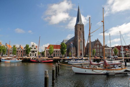 Old wooden sailing boats mooring at Zuiderhaven (Southern harbor) in Harlingen, Friesland, Netherlands, with Aartsengel Michael Kerk church 