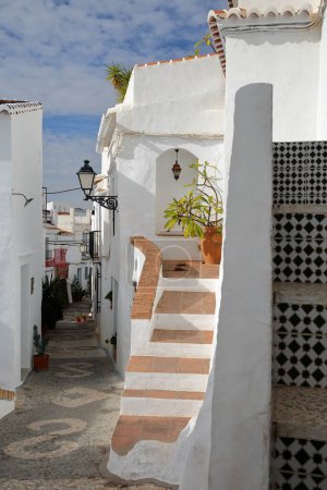 A picturesque narrow cobbled alley in Frigiliana, Axarquia, Malaga province, Andalusia, Spain, with traditional whitewashed little houses and a decorated cobbled pavement
