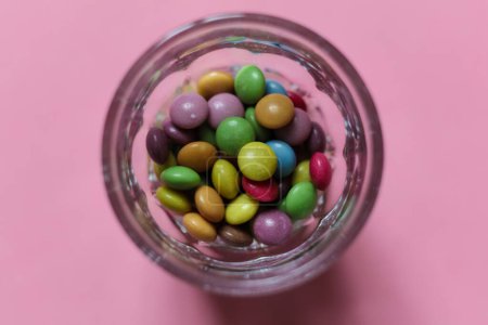 a glass full of colorful candy on pink background