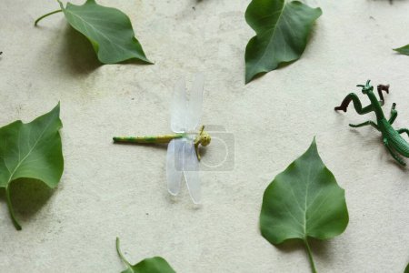 Grüne Blätter und Spielzeuginsekt auf altem Papierhintergrund. Flache Lage.
