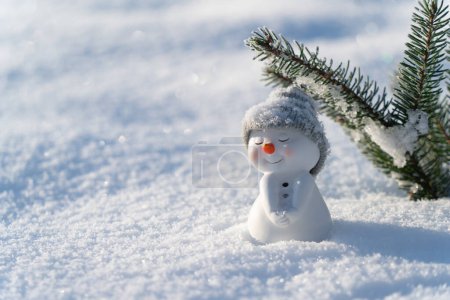 Téléchargez les photos : Figure de petit bonhomme de neige mignon dans un chapeau tricoté et écharpe sur un champ enneigé par une journée d'hiver ensoleillée. Concept pour tête de site d'hiver carte de mockupcard ou carte de Noël. - en image libre de droit