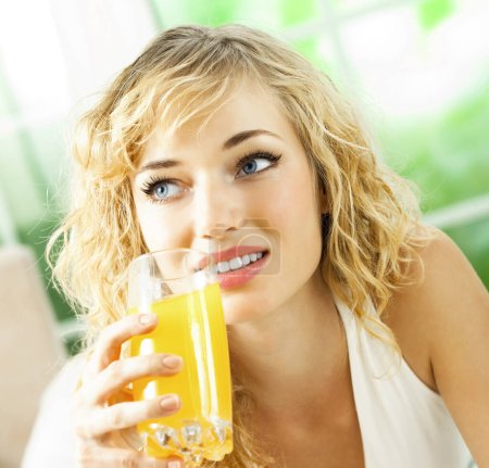 Foto de Retrato de feliz sonriente joven hermosa rubia bebiendo jugo de naranja - Imagen libre de derechos