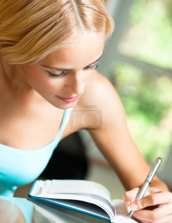 Téléchargez les photos : Jeune belle femme blonde étudiant avec ordinateur portable ou organisateur, à l'intérieur - en image libre de droit