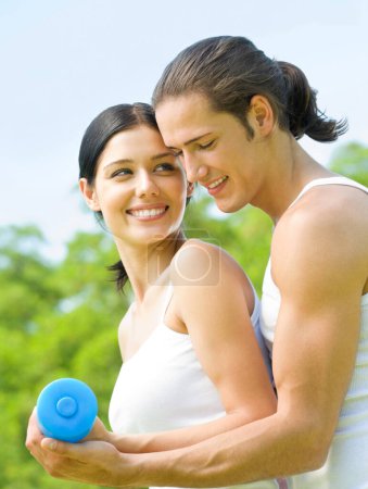 Téléchargez les photos : Joyeux jeune couple souriant avec haltères sur l'entraînement de fitness en plein air - en image libre de droit