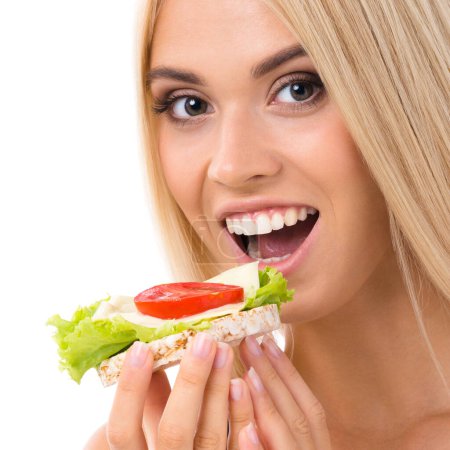 Téléchargez les photos : Femme en tenue de sport mangeant un sandwich végétarien, isolée sur fond blanc. Jeune mannequin blond sportif au studio tourné. Santé, beauté et régime alimentaire concept. - en image libre de droit