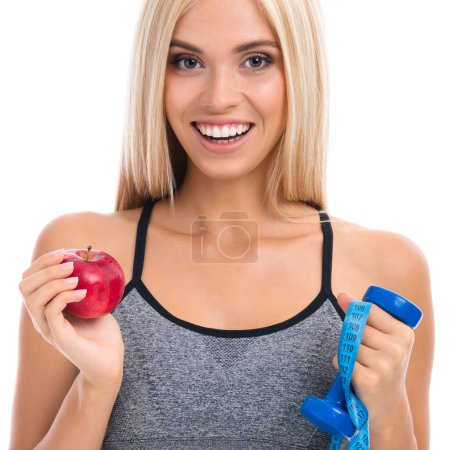 Photo for Woman in sportswear with tape measure, dumbbell and apple, isolated over white background. Young sporty blond model at studio shot. Health, beauty and fitness concept. - Royalty Free Image