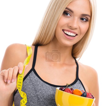 Photo for Woman in sportswear with tape measure and fruits, isolated over white background. Young sporty blond model at studio shot. Health, beauty and fitness concept. - Royalty Free Image