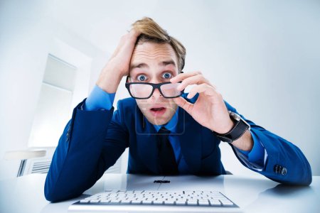 Shocked or surprised businessman in blue suit and glasses, working with computer at office. Success in business, job and education concept.