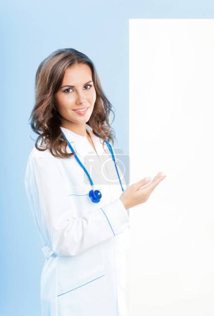 Photo for Portrait of happy smiling young female doctor showing blank signboard, over blue background - Royalty Free Image