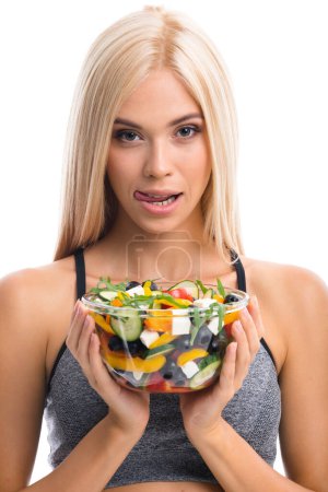 Photo for Woman in sportswear with plate of salad, isolated over white background. Young sporty blond model at studio shot. Health, beauty and fitness concept. - Royalty Free Image